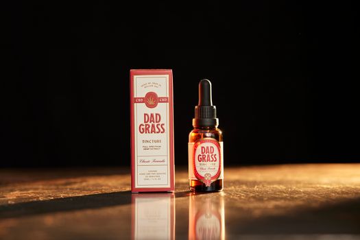 Close-up of Dad Grass full spectrum CBD tincture bottle and box on a warm wooden surface.