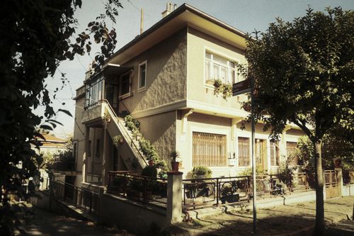 Free A vintage-style two-story house with exterior stairs surrounded by trees and plants. Stock Photo