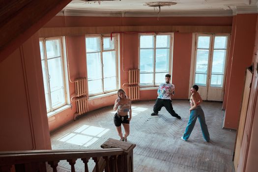 Three diverse dancers performing in a bright, empty room with wooden flooring.