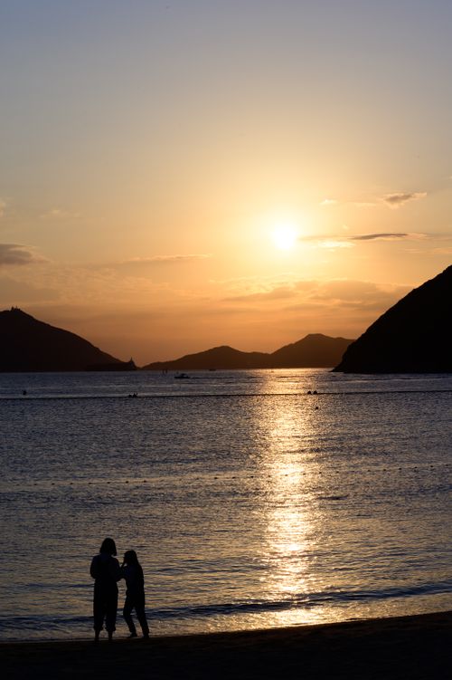 Free Silhouettes on a serene beach at sunset with tranquil waters and a golden sky. Stock Photo