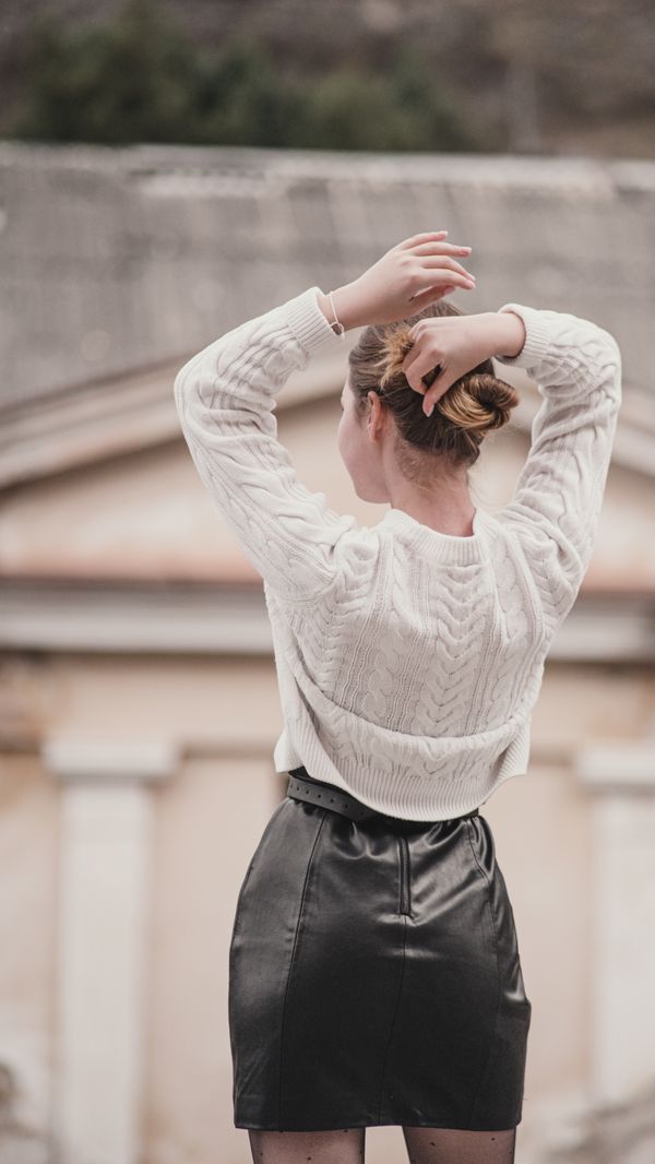 woman in cream cable-knit sweater and black leather mini skirt with ankle boots