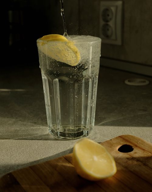 Free Fresh lemon slice splashes into a glass of water on a kitchen counter. Stock Photo