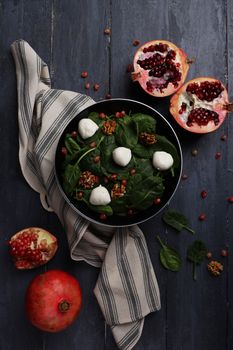 A vibrant flat lay of a spinach salad with pomegranate and mozzarella on a rustic table.