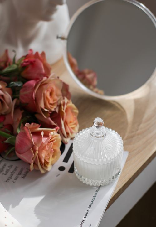 Free Aesthetic arrangement of roses, elegant glass jar, and mirror on a wooden surface for a calming ambiance. Stock Photo