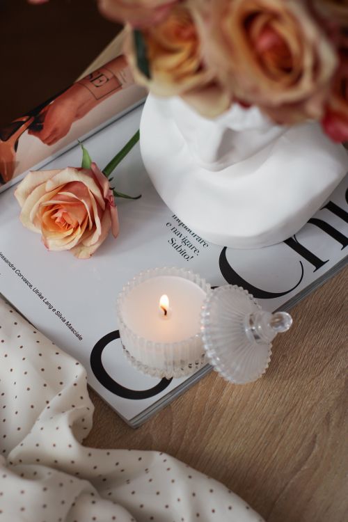 Free Captivating still life featuring a lit candle, a rose, and chic magazine on a wooden table. Stock Photo