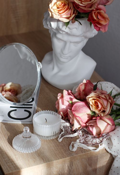 Free Artistic arrangement featuring roses, a bust sculpture, mirror, and candle on a wooden table. Stock Photo