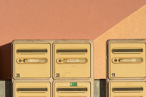Free Close-up of yellow mailboxes against a textured pink wall with numbers visible. Stock Photo