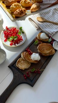 Appetizing stack of pancakes with cream and fresh berries served on a wooden board with sunlight casting a warm glow.