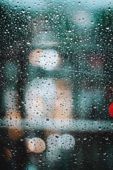 Raindrops on glass with blurred city lights in background, creating a bokeh effect.