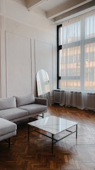 Elegant minimalist living room with large windows and cozy furnishings.