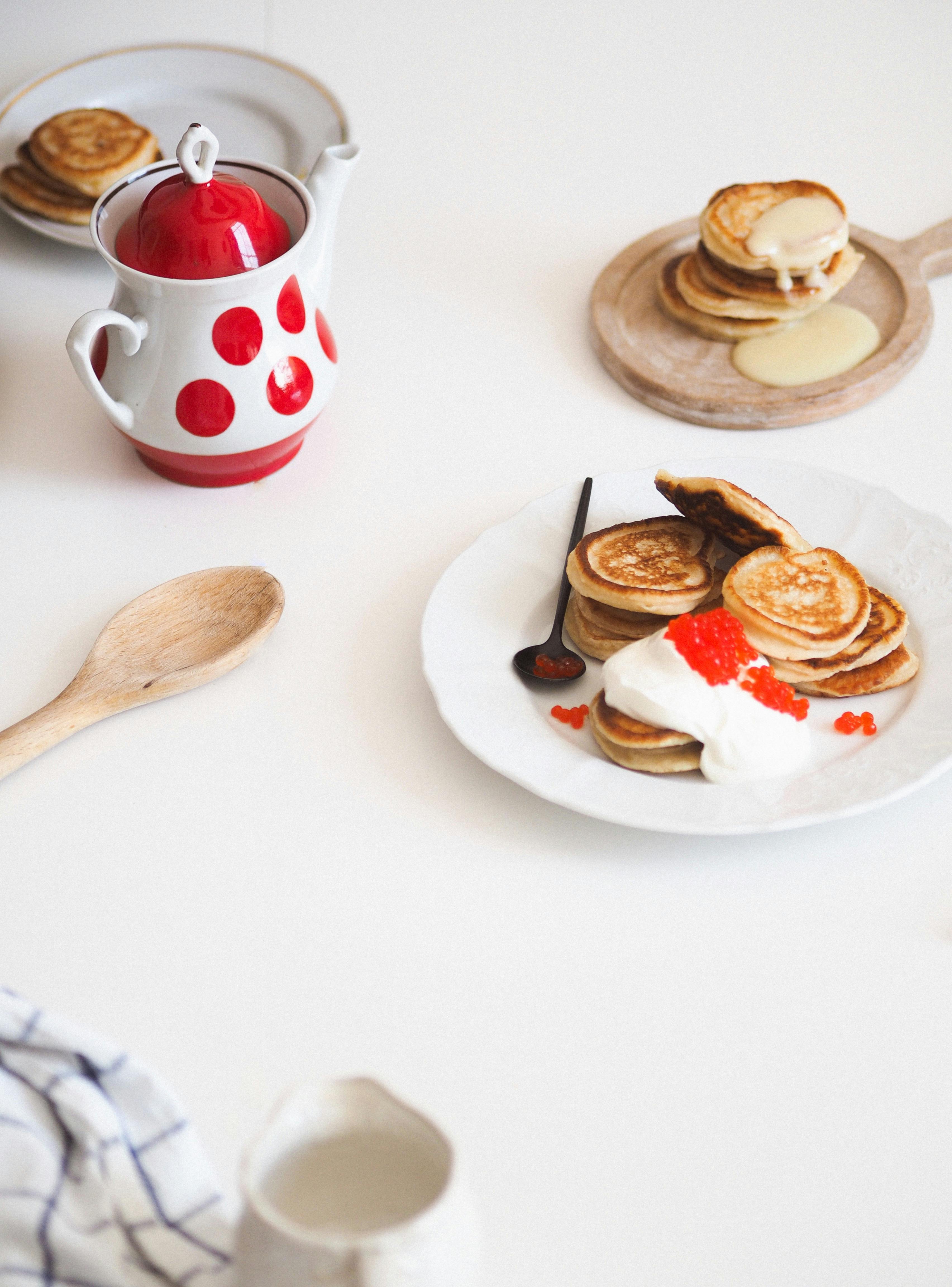 A beautifully styled pancake breakfast with fresh cream and berries on a minimalist table setting.