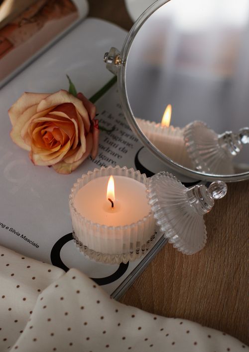 Free Elegant setting showcasing a glowing candle, rose, and mirror reflection on a magazine. Stock Photo