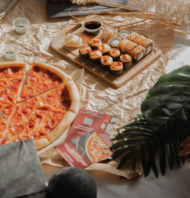 Pizza And Sushi Rolls On Wooden Chopping Board