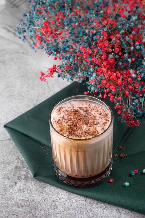 Free Glass of hot chocolate on green napkin with colorful flowers for a cozy vibe. Stock Photo