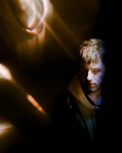 Young Man in a Hoodie Standing in the Dark with His Face Illuminated by a Spotlight 