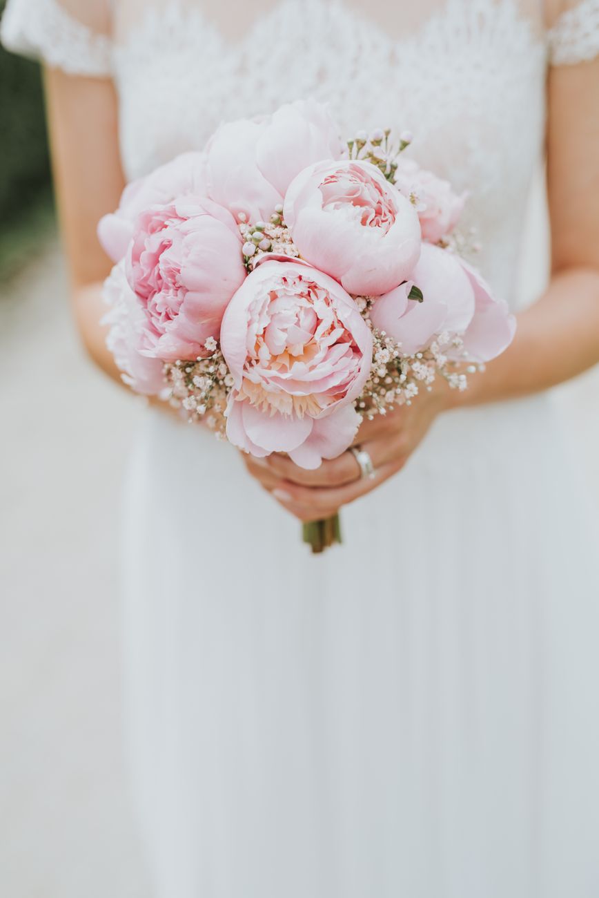 Bride holding a beautiful bouquet of pink peonies, perfect for a romantic wedding setting.