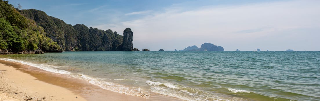 Serene beach view in Thailand with ocean waves and lush cliffs.
