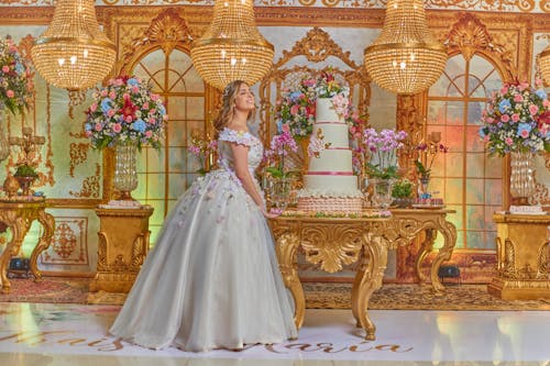 Free A Happy Young Woman in a Gown Standing by a Cake Stock Photo