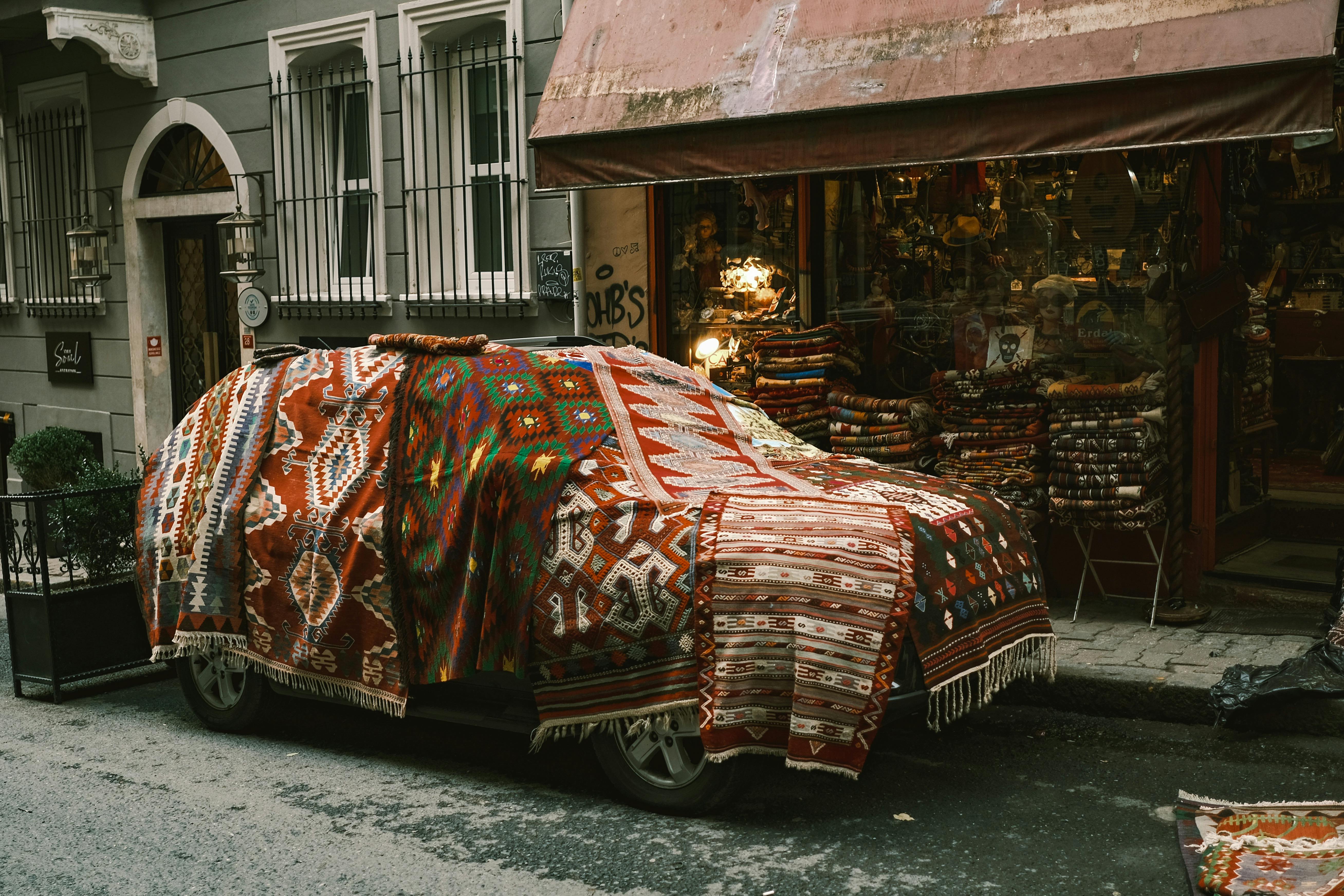 A parked car is fully covered by traditional Turkish rugs on a city street.