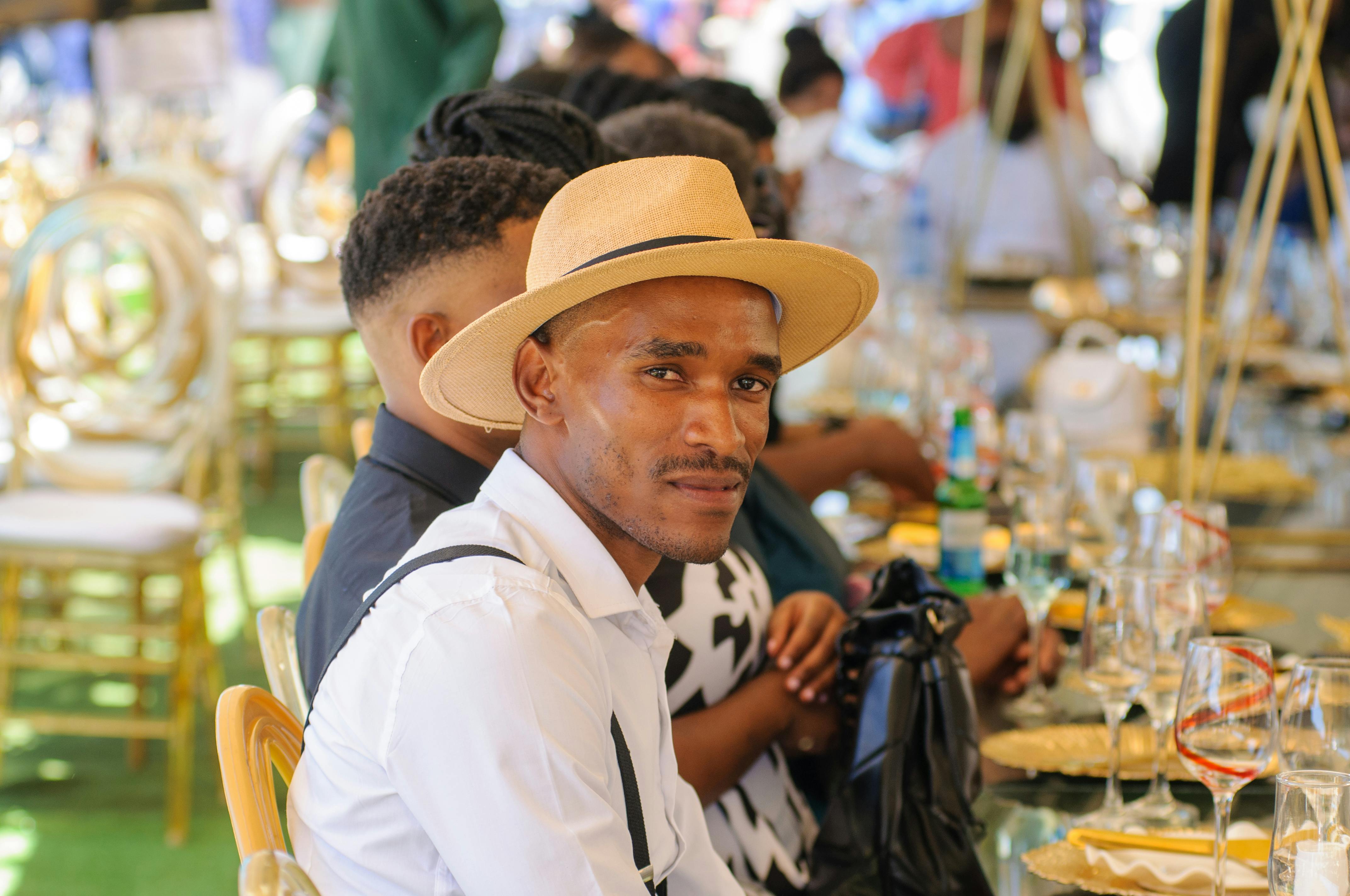 Man in a hat at a stylish outdoor event, amidst elegant table settings and guests.