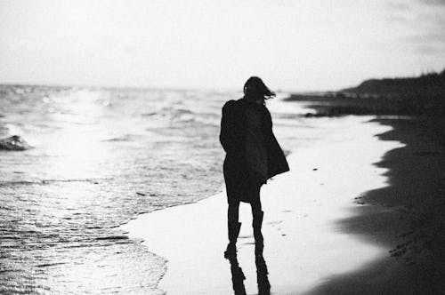 Black and White Photo of a Person Walking in the Beach