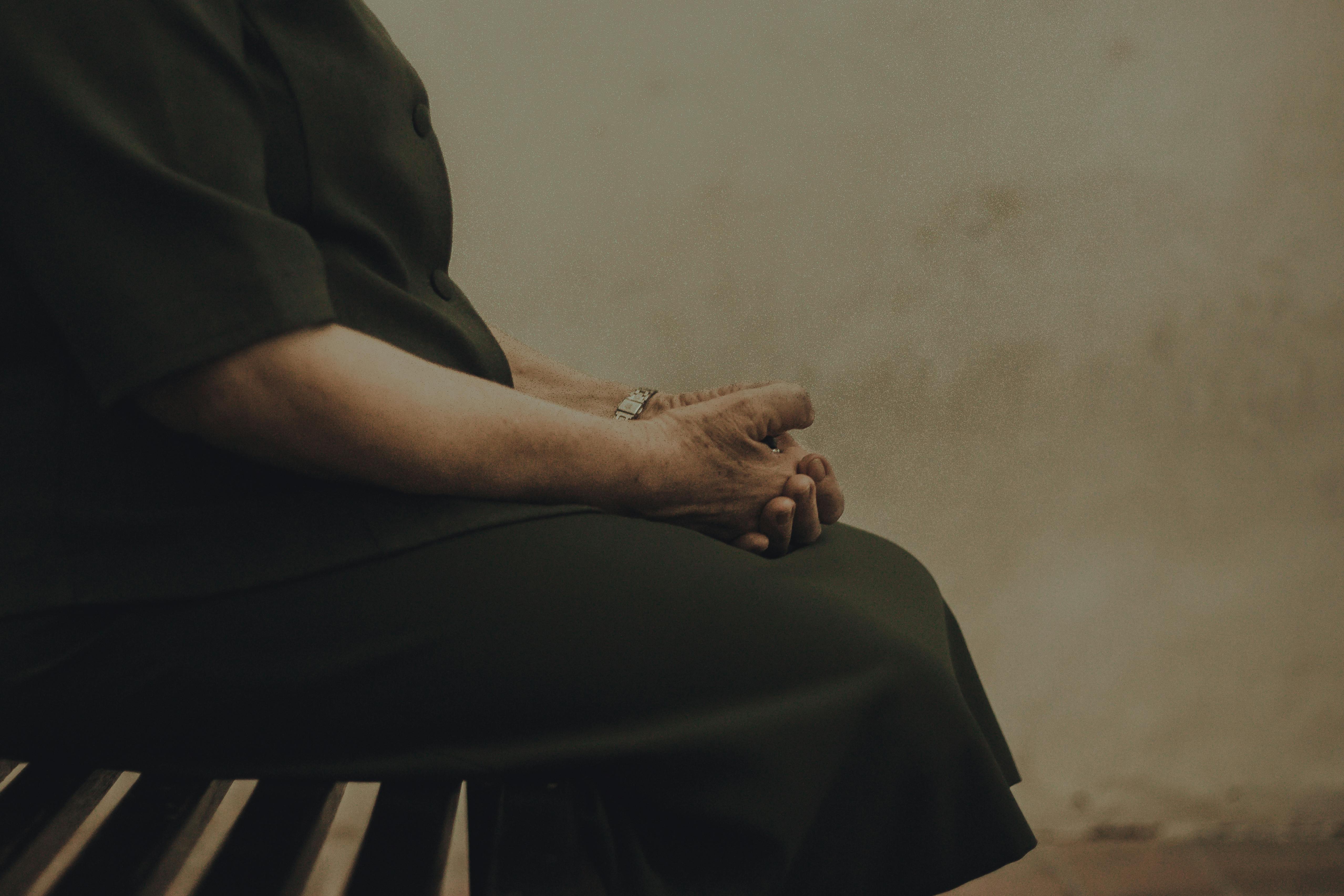 Close-up of an elderly woman sitting on a bench, hands clasped, creating a contemplative mood.
