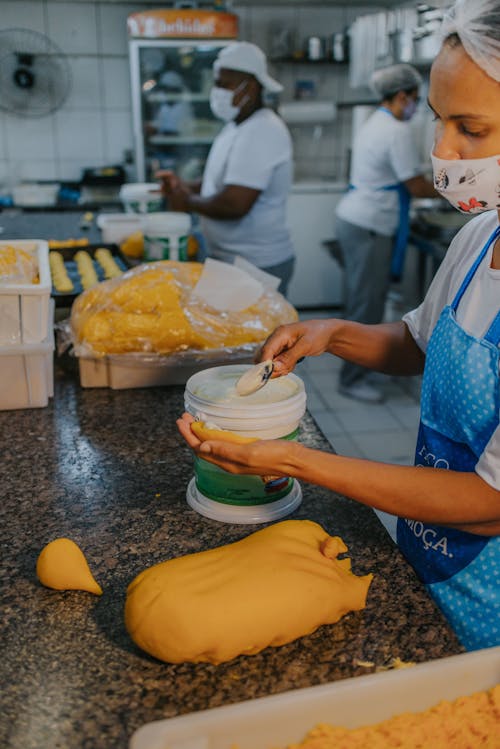 Free Person with Face Mask Putting Filling on a Dough
 Stock Photo
