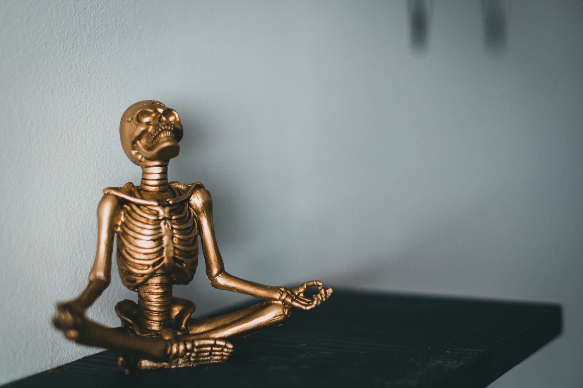 冥想教學如何重塑大腦:神經科學證據與可塑性益處 A golden skeleton statue sits in a meditative pose on a black surface against a neutral background.