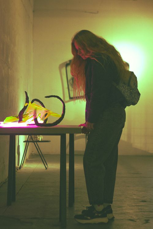 Free A woman stands in a dimly lit room, observing neon art on a table. Stock Photo