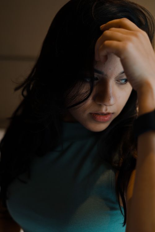 Free A young woman with dark hair leans on her hand, introspective in soft light. Stock Photo