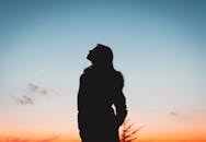 一个女人剪影映衬在生机勃勃的日落天空下，唤起平静与沉思