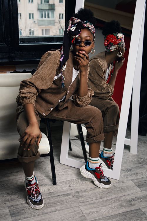 Free Trendy woman in retro attire with vibrant sneakers poses in a studio mirror reflection. Stock Photo