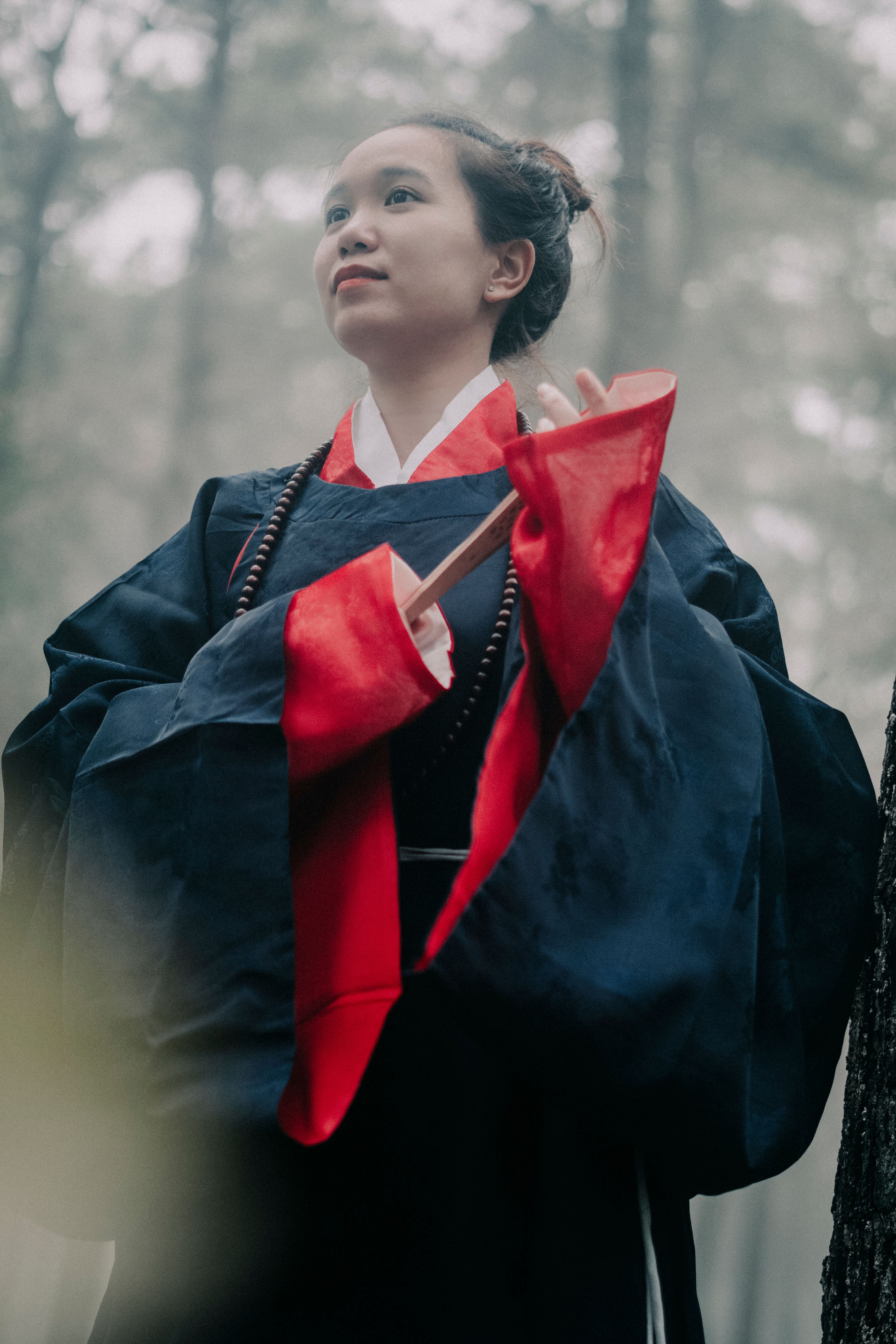 Asian woman wearing traditional clothing in a misty forest, creating an ethereal mood.
