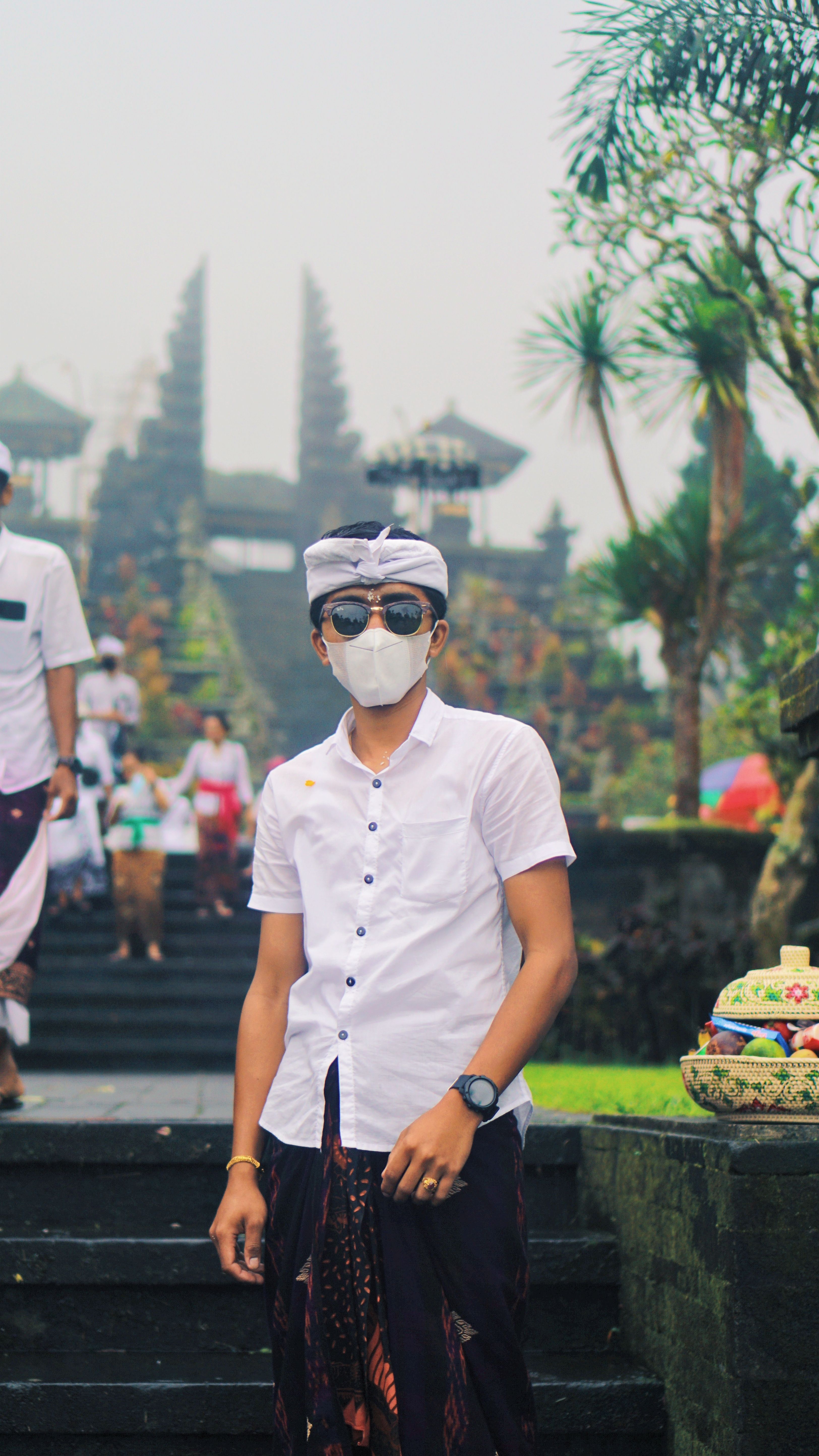 A young man in a mask and sunglasses poses at a temple in Bali, Indonesia.
