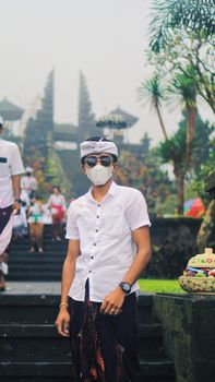 A young man in a mask and sunglasses poses at a temple in Bali, Indonesia.