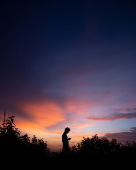 Silhouette of a person under a vibrant twilight sky with orange and blue hues in KL, India.. silhouette, person, under