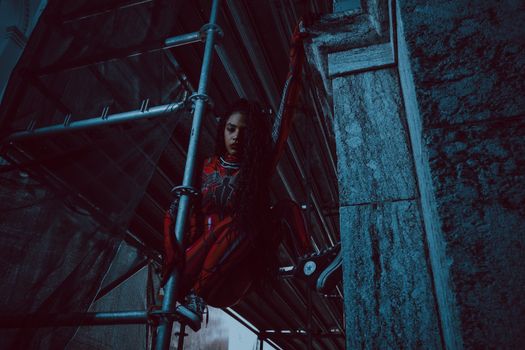 A woman in a Spider-inspired costume clings to scaffolding, showcasing strength and agility.