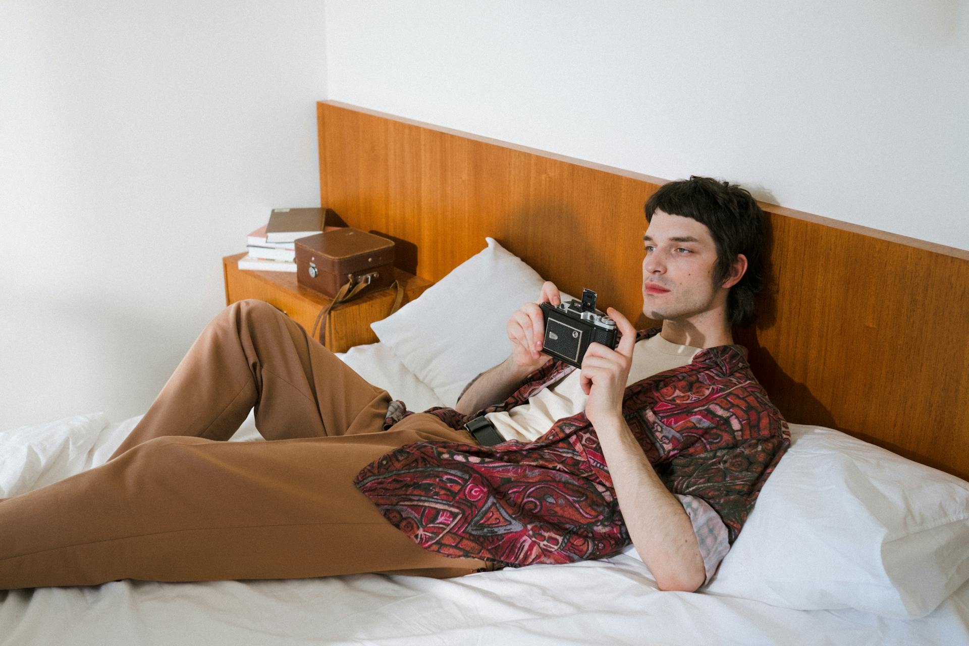 A Male Laying on Bed and Holding an Analog Camera 