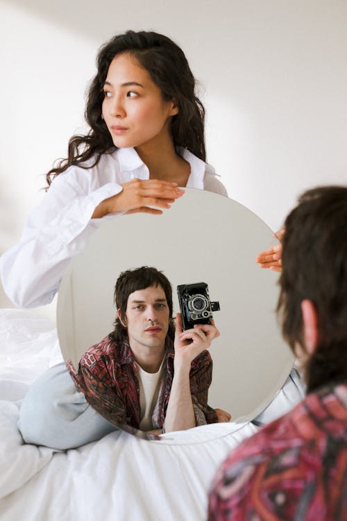 A Male Holding an Analog Camera and Looking at Camera and Female Holding a Mirror While Photoshoot