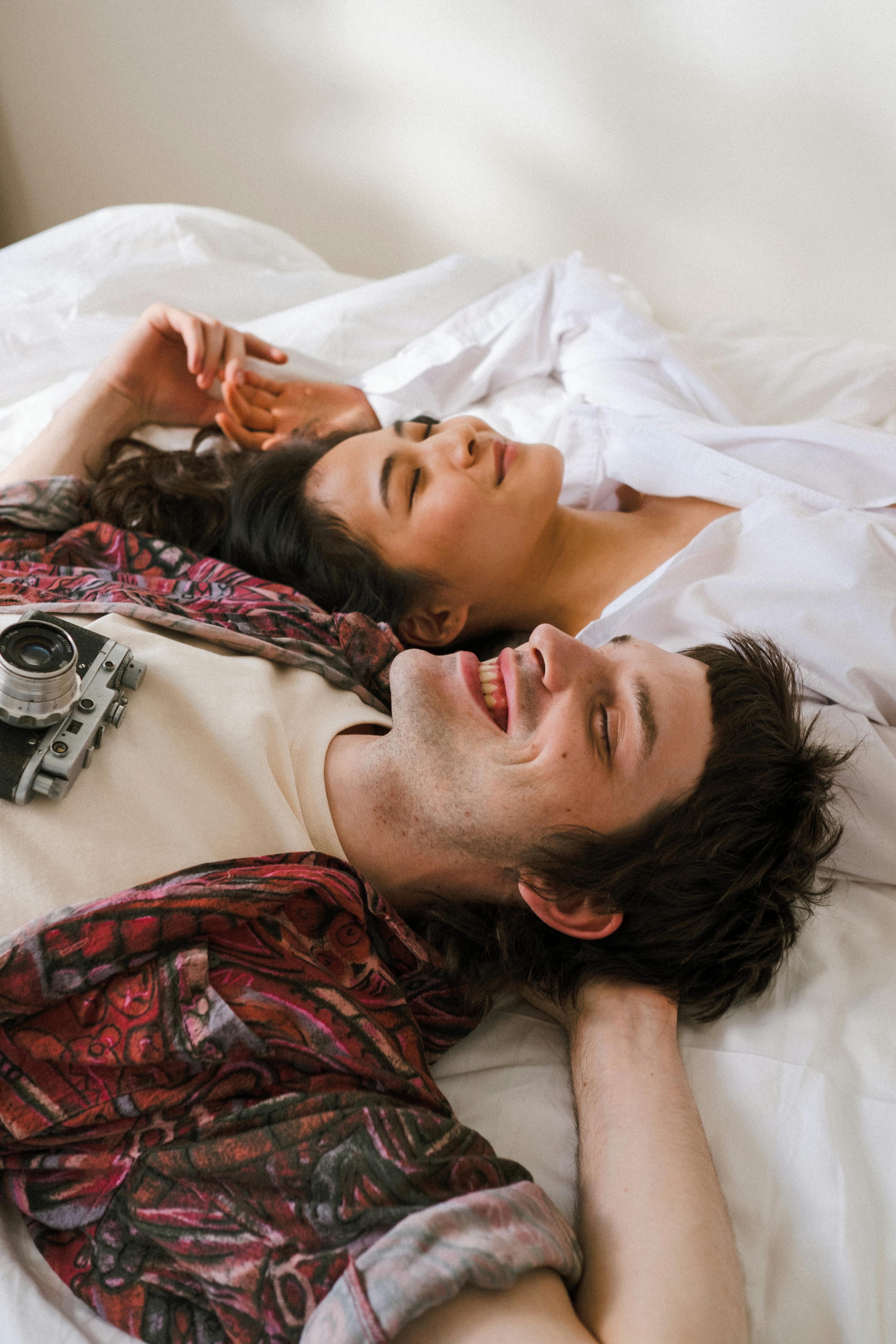 A couple relaxes happily on a bed, showcasing diverse young love and peaceful moments indoors.