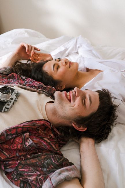 A couple relaxes happily on a bed, showcasing diverse young love and peaceful moments indoors.
