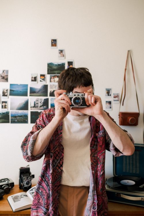 Free A young man using a vintage camera indoors, with creative decor and retro vibe. Stock Photo