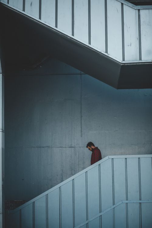 Free A man in a red shirt descends a modern staircase indoors with a minimalist architectural design. Stock Photo