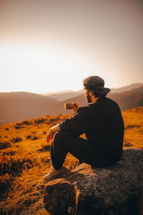 Free A Man Sitting on a Rock Looking at the Scenic View of the Sunset at the Mountain Stock Photo