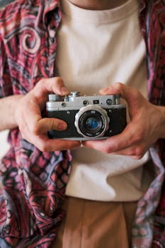 Midsection of an adult holding an analog vintage camera wearing casual clothing.