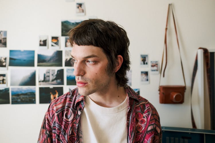 Young Man At Home With Photos On Wall And Vintage Camera In Background