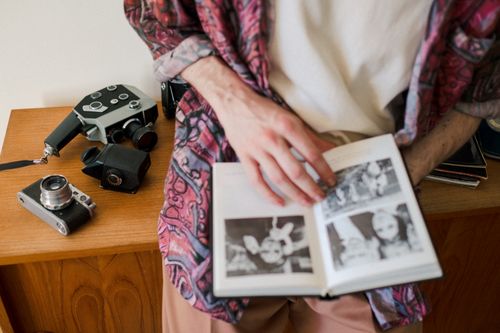 Free Man in casual attire flipping through a classic photo album beside vintage cameras at home. Stock Photo