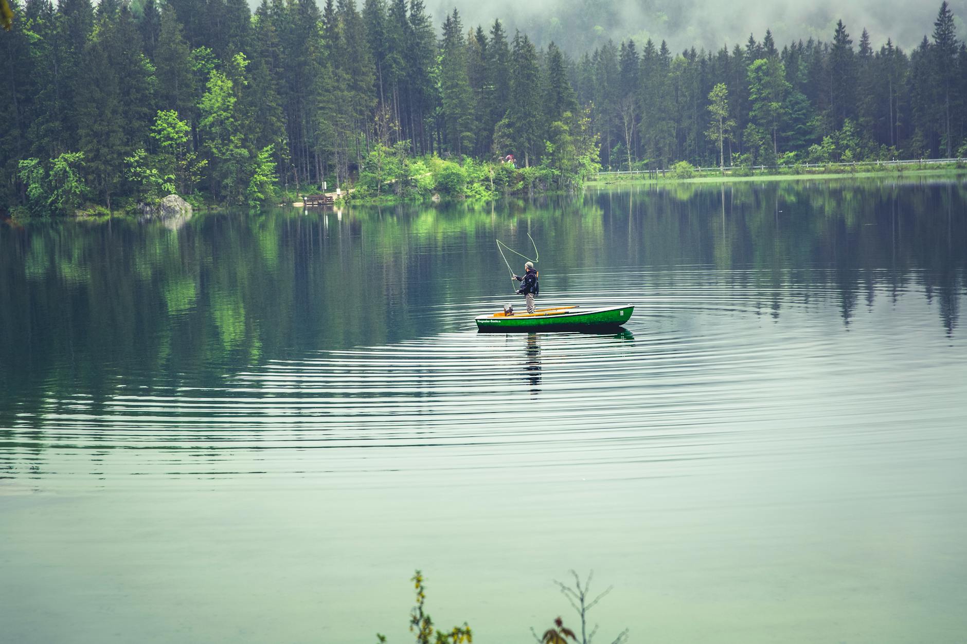 Man inside the boat is fishing at the middle of the lake