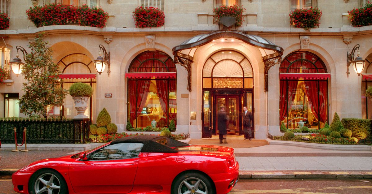Red sports car parked outside a lavish hotel entrance at night, showcasing opulence.