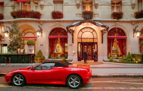 Red sports car parked outside a lavish hotel entrance at night, showcasing opulence.